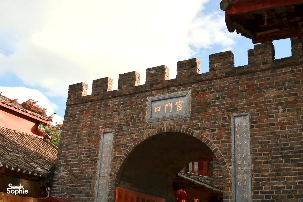 Brick archway in Lijiang’s Old Town, marked with Chinese characters, framed by shop eaves during a guided walk in Shuhe