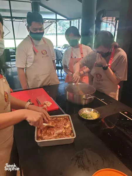 Colleagues in aprons plating and seasoning dishes around a shared stove at a Taiwanese night market cook-off for team building Singapore