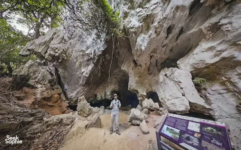 Traveller stands inside a rock cave at Kubang Badak, Langkawi, near a handrail and trail sign on the guided tour
