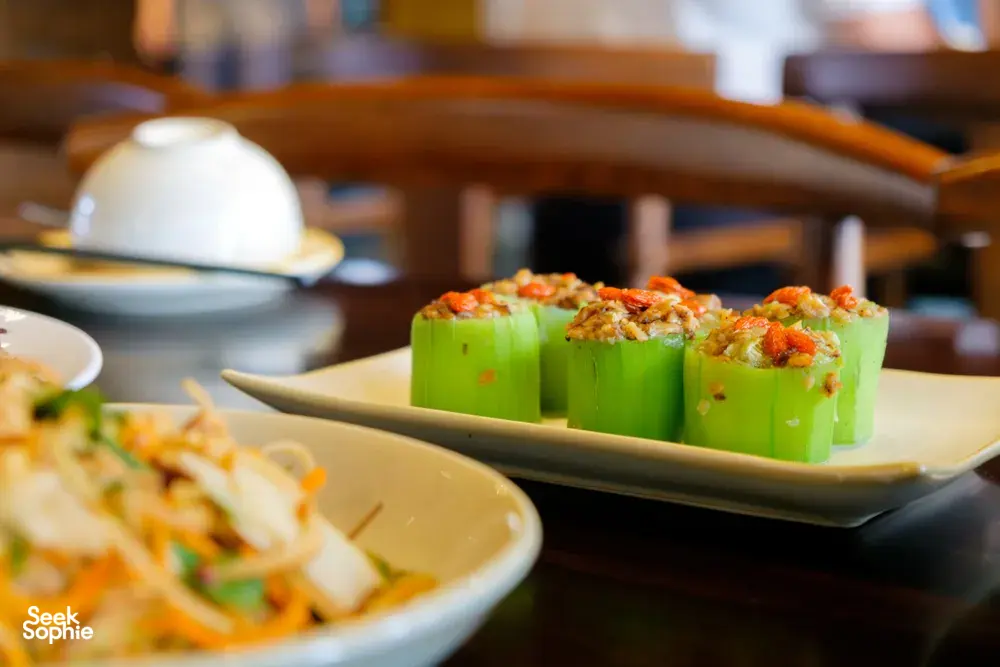 Stuffed green gourd pieces topped with herbs on a serving tray, with other dishes at an indoor Hanoi tasting meal
