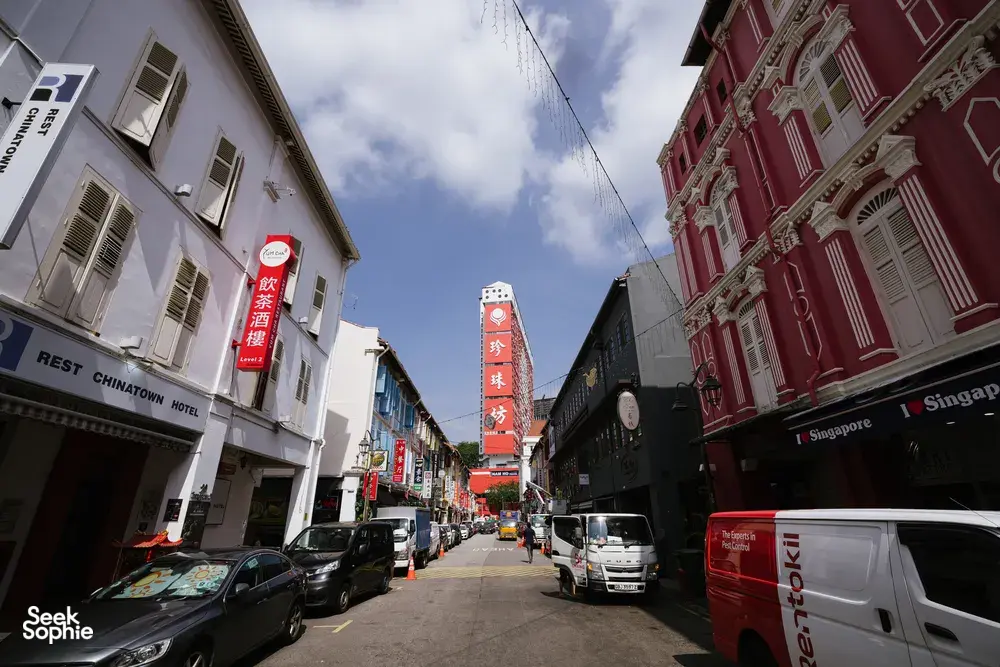 Singapore Chinatown street with shopfronts, parked cars and red heritage buildings, as a team explores alleys to find Singapore hidden gems