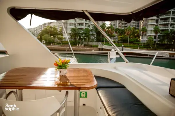 Lounge area on a 57ft yacht with a wooden table and flowers, overlooking Singapore waterfront en route to Lazarus Island