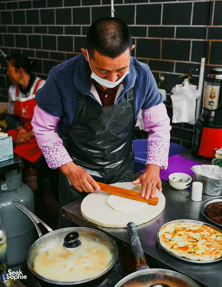 Local cook presses dough on a griddle for a Lijiang food hunt with local stories, in a Yunnan back-kitchen