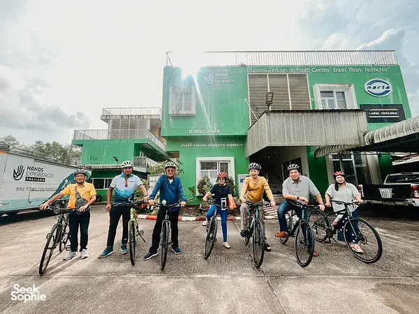 Helmeted cyclists posing outside a Hands Experiences Thailand centre in Khao Lak, ready for a half-day cycling and rafting trip