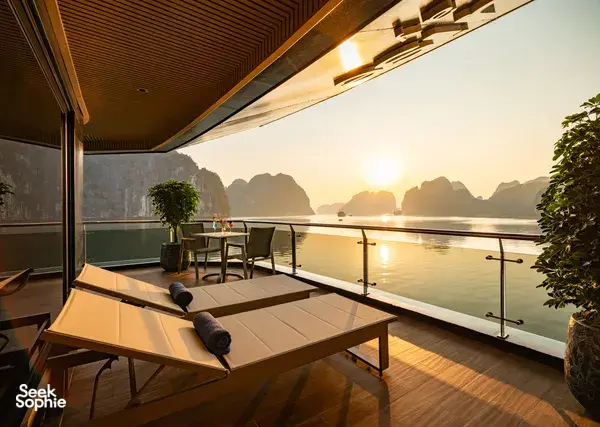 Private spa sun lounger on a Doris Cruise balcony overlooking Halong Bay at sunrise, with limestone karsts in the distance