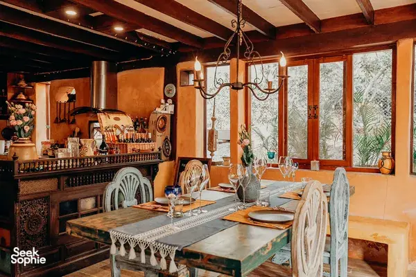Warm Chiang Mai dining space for a home cooking class, with set chef’s table, chandelier, and windows opening onto greenery.