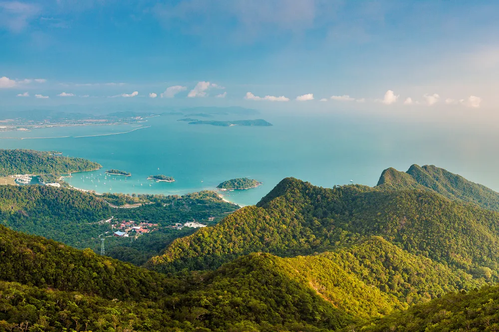 Panoramic view over forested hills and a sheltered bay on Langkawi, with islands and boats in the blue sea