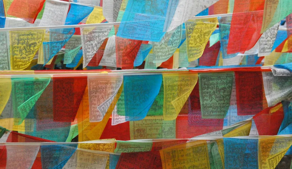 Multicoloured prayer flags strung overhead, fluttering in a mountain breeze above a narrow road and stone walls