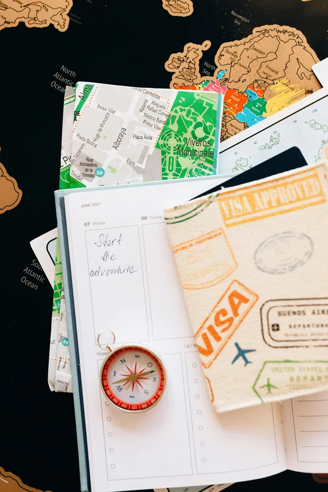 Travel journal open with a compass, passports, and folded maps on top of a world map background, capturing hands-on trip planning