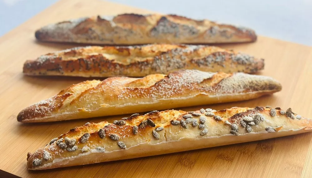 Golden, flour-dusted baguettes on a wooden board, close-up of fresh bread for Food & Drink in Singapore.