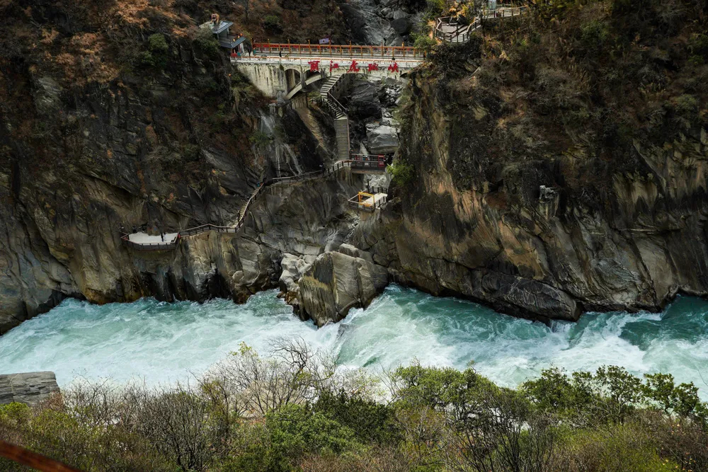 Riverside gorge with foaming turquoise rapids and a long walkway over the water beside tall canyon walls