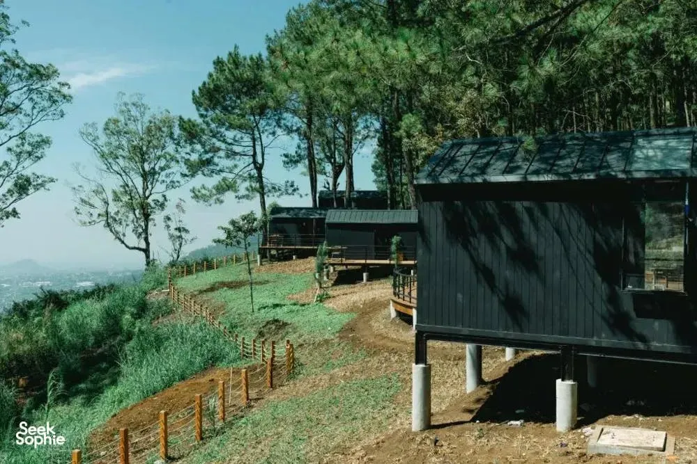 Wooden eco-lodge cabin and deck in a forested hillside setting, overlooking a misty valley beyond the trees