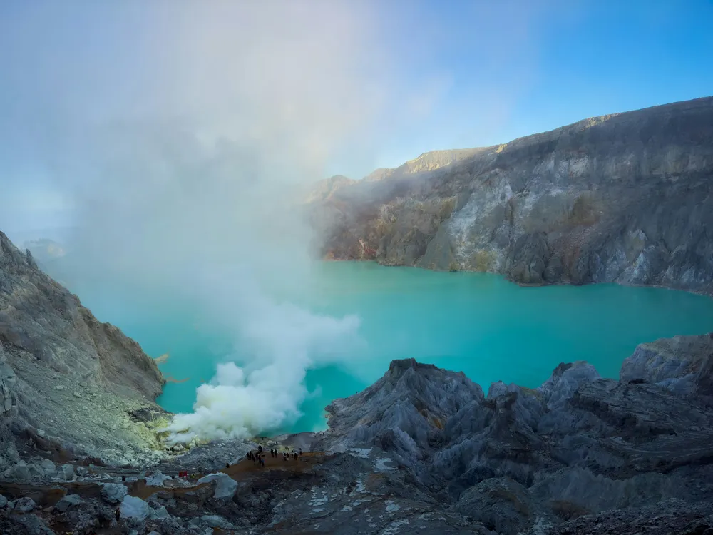 Turquoise crater lake steaming below from the rocky rim, with hikers in Banyuwangi at a quiet dawn, Mt Ijen