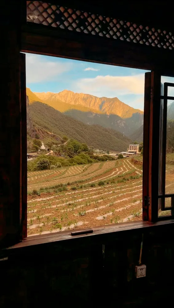 View from an open doorway onto terraced farmland and a mountain landscape at sunrise, framed by rustic wooden beams