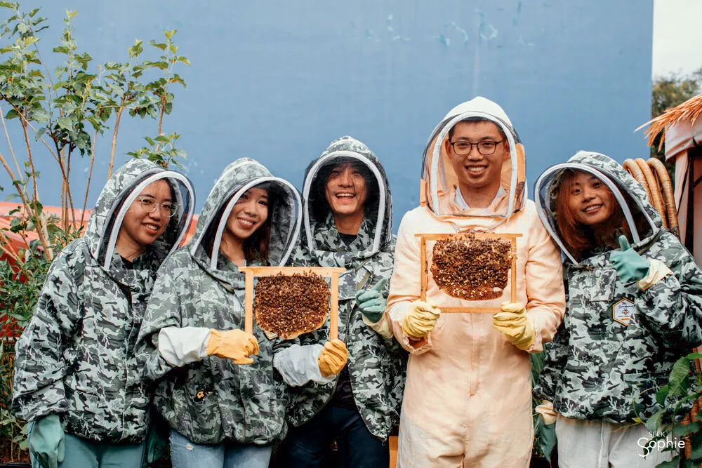 Smiling beekeepers in protective suits holding honeycomb frames together outdoors during a Secret Urban Farm visit — Singapore hidden gems