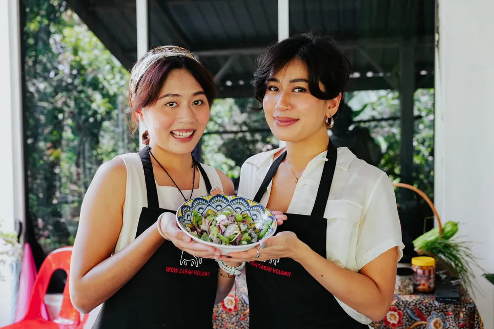 Apron-clad students presenting a colourful bowl of salad at an outdoor cooking class in Kota Kinabalu