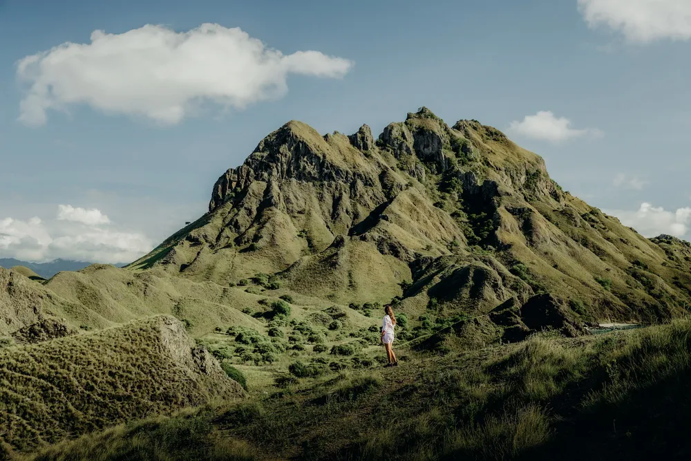 A lone hiker pauses on a grassy ridge overlooking rugged hills in Komodo National Park near Labuan Bajo