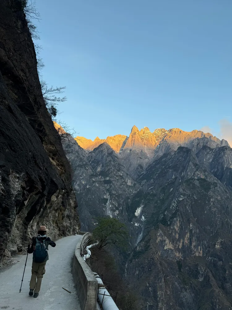 Hiker with backpack walks along a narrow mountain path between cliffs at golden sunrise, with steep valleys stretching ahead