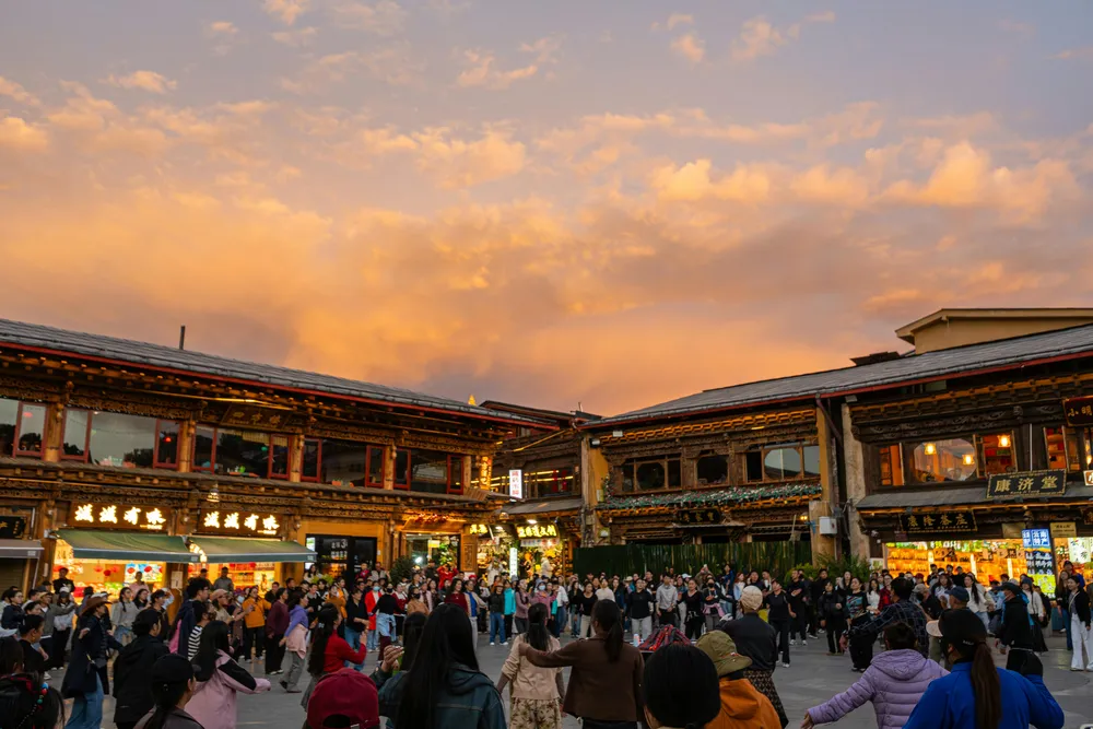 Crowds stroll through a lively old-town market street lined with traditional wooden shopfronts and lantern lights at dusk