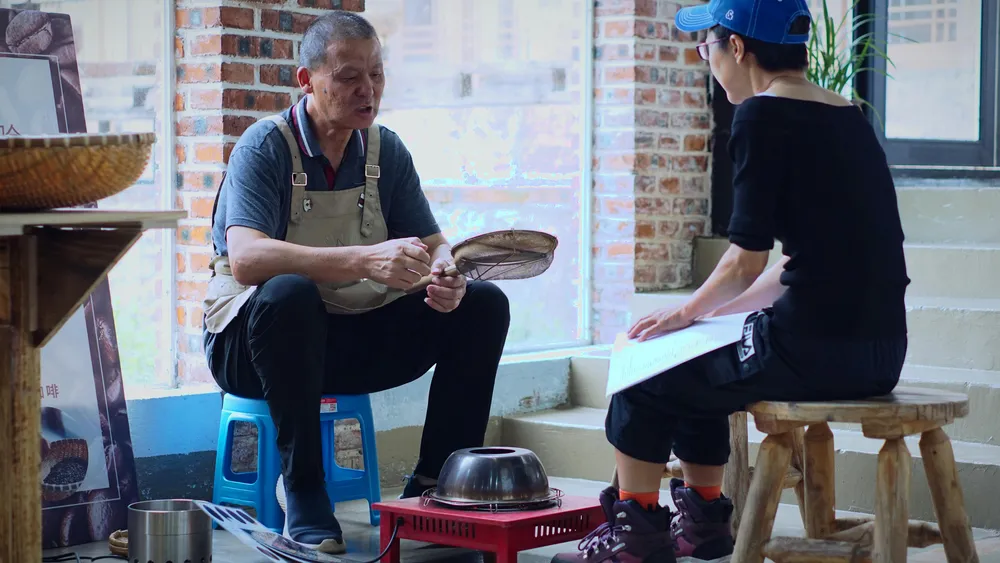 Ayah Phoebe sedang mengajar seorang pelajar cara menyangrai biji kopi secara manual. Beliau percaya cara terbaik untuk belajar ialah cara tradisional — perlahan-lahan, dengan tangan.