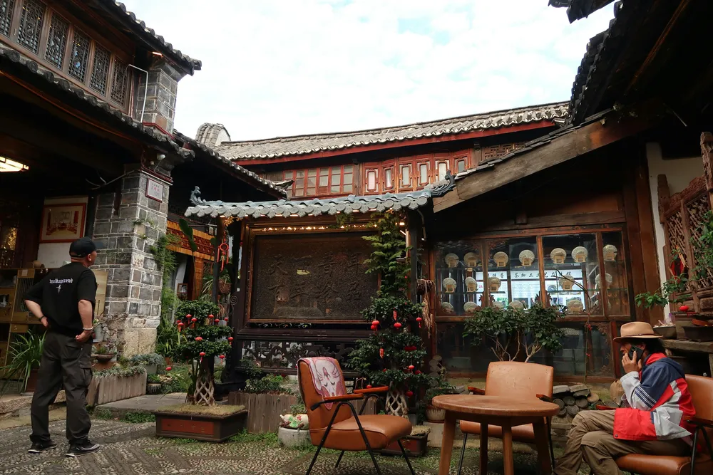 Traditional courtyard with stone and timber buildings, potted flowers and a seating area, with a few people gathered outside