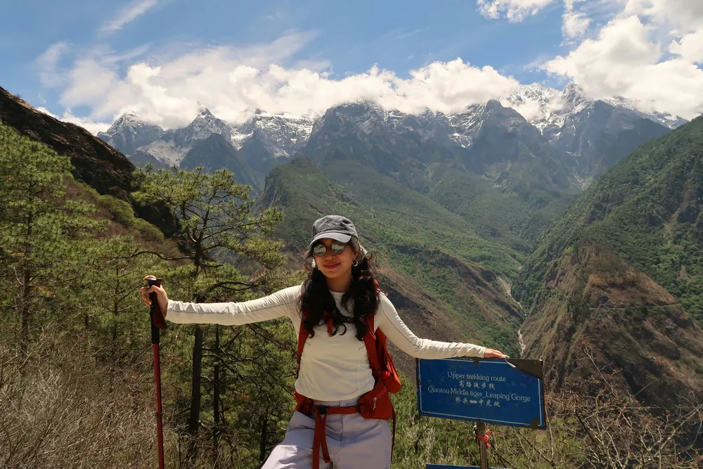 Hiker posing outdoors with a trekking pole in front of a vast mountain panorama, snowy peaks and green valleys