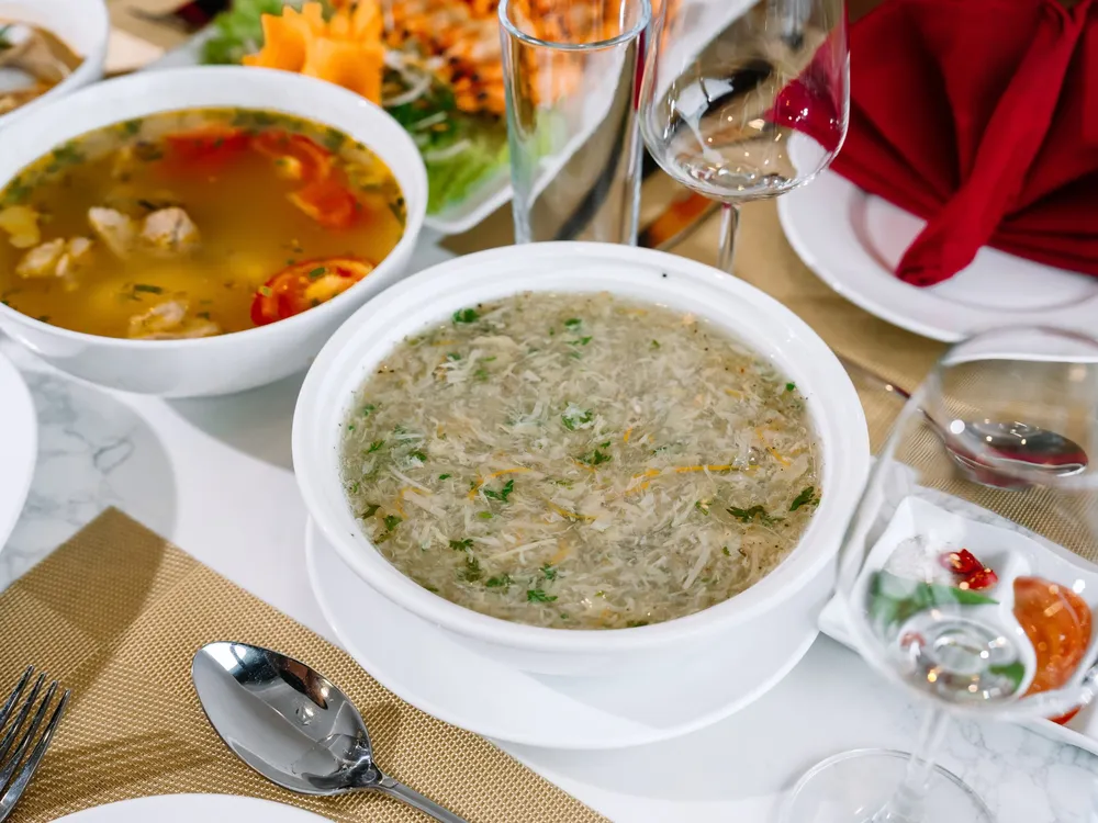 Cat Ba cruise dinner table with individual soup bowls and fresh herbs, set for a luxe 2D1N dining service