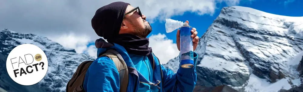 Winter hiker in a beanie and jacket taking a sip from a bottle against snowy mountain peaks, with a “FACT?” badge overlay