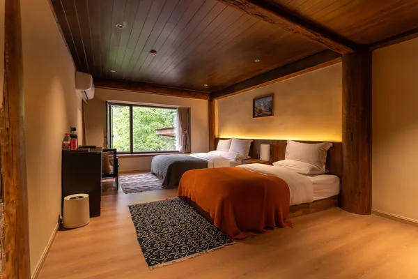 Quiet wooden guest room in Shangri-La with two neatly made beds, warm lighting, and a small rug by the windows