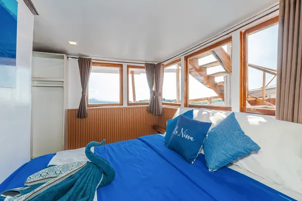 La Famille cabin berth with blue quilt and ocean-view windows, ready for a Komodo boat trip, Labuan Bajo