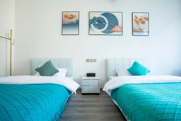 The Bivou Lijiang twin guest room with crisp white beds and turquoise quilts, plus framed coastal artwork for a 2D1N stay