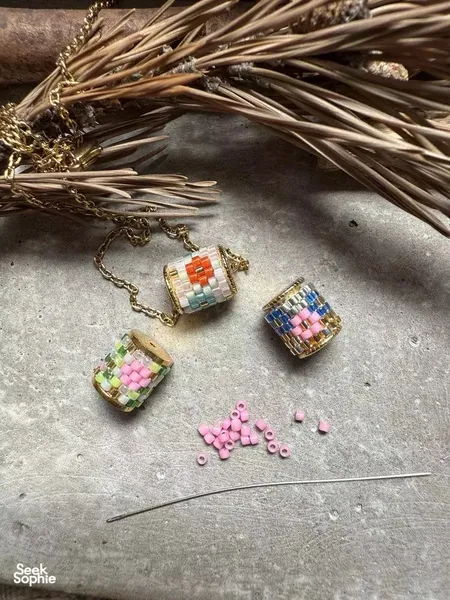 Close-up of three colourful beaded bracelets and stray beads with straight pins on a concrete tabletop for jewellery making