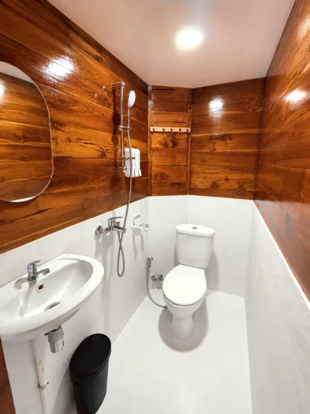 Wood-lined phinisi bathroom with toilet, sink and shower fittings on white surfaces, part of the shared 3D2N Komodo cruise in Labuan Bajo
