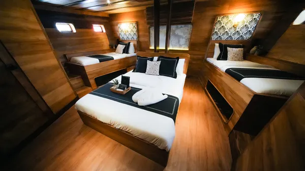 Angelica Liveaboard phinisi cabin view with three neatly made beds, patterned headboards, and polished wooden flooring
