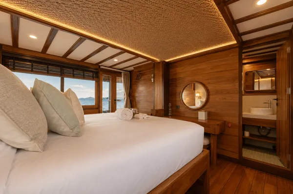 Cozy phinisi suite interior with a large double bed and compact en-suite bathroom on a trip to Komodo Island