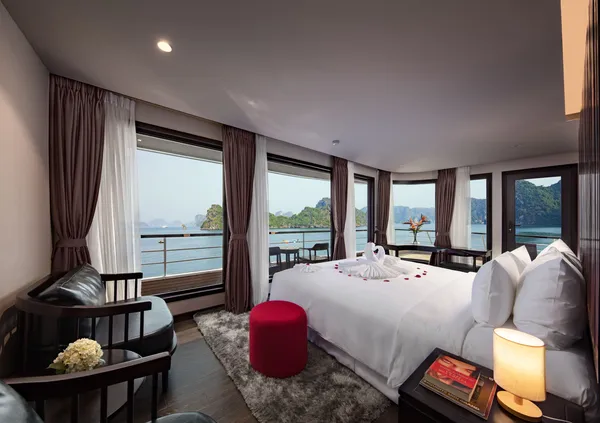 Red pouf and cosy seating by the window as the bed faces the sea on an Oasis Bay Party Cruise room in Halong Bay