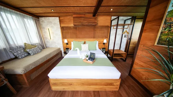 Wooden phinisi cabin interior with a made-up double bed, canopy curtains, and lounge seating, on a Komodo Island cruise