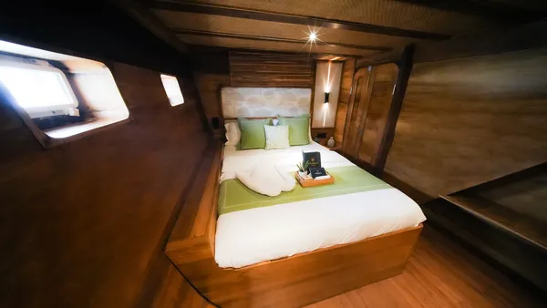 Cozy narrow phinisi cabin with a sunken-feel double bed and bedside tray for the 3D2N Komodo cruise—sunset BBQ and jacuzzi in Labuan Bajo