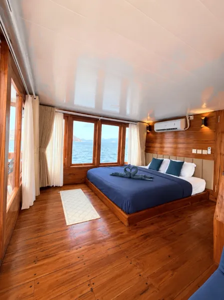 Wooden phinisi suite with a king bed, air-conditioning and curtain-framed sea view on a 3D2N shared cruise from Labuan Bajo, Komodo Island