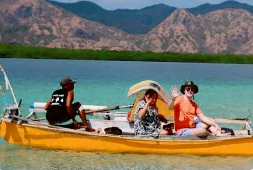 Travellers relaxing on an orange boat in calm turquoise water with mountains in the background near Labuan Bajo