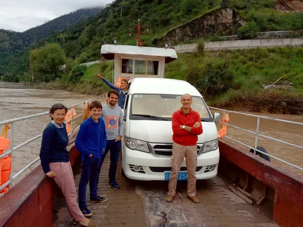 Para pengembara bergambar di sebelah van mini putih di atas feri yang menyeberangi sungai, bersama pemandu Ciel Yunnan berhampiran Dali