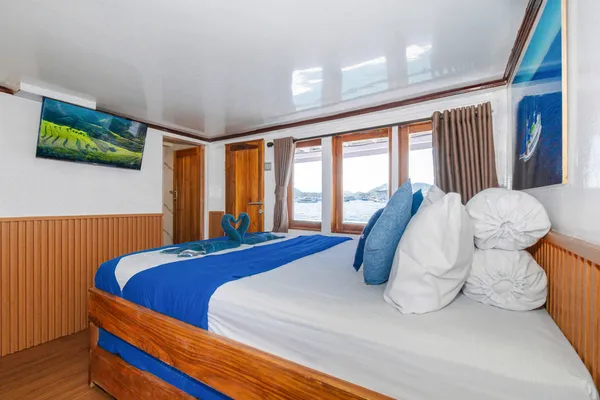 Bed in a wooden cabin with folded towels aboard La Famille 3D2N Komodo boat trip onboard in Labuan Bajo