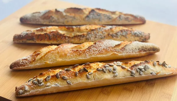 Golden, flour-dusted baguettes on a wooden board, close-up of fresh bread for Food & Drink in Singapore.