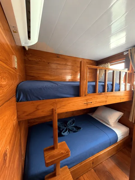 Wooden phinisi cabin bunk beds with dark-blue bedding and storage, inside the shared 3D2N Komodo cruise in Labuan Bajo