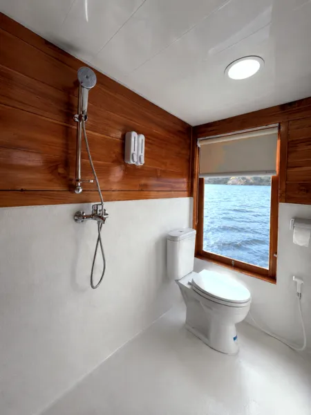 Phinisi bathroom with sink, shower and toilet beside a porthole window on a 3D2N Komodo cruise, Labuan Bajo