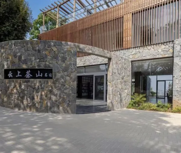 Stone-walled entrance of a tea lodge in Xishuangbanna, with a courtyard path and a Chinese sign on the screen