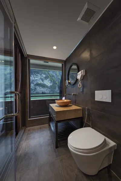 Modern bathroom on the Oasis Bay Party Cruise with a vanity, mirror and toilet, framed by Halong Bay cliffs