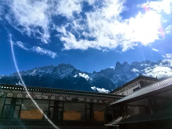 Traditional Naxi-style courtyard at The Bivou Lijiang in Shuhe Ancient Town, with mountain silhouettes and sun rays through clouds