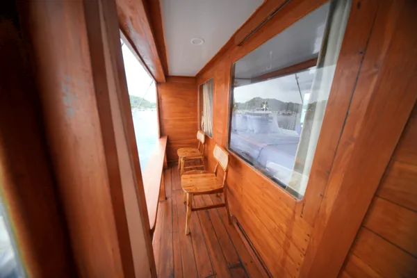 Wooden boat passageway with a single chair by the window, daylight streaming in over the deck for a 3D2N Komodo trip Labuan Bajo