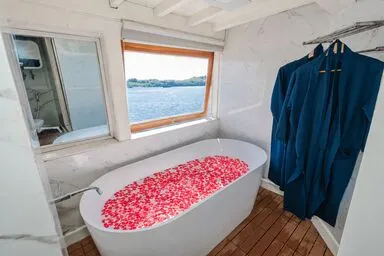 Petal-covered bathtub by the window with ocean view aboard La Famille 3D2N Komodo boat trip in Labuan Bajo